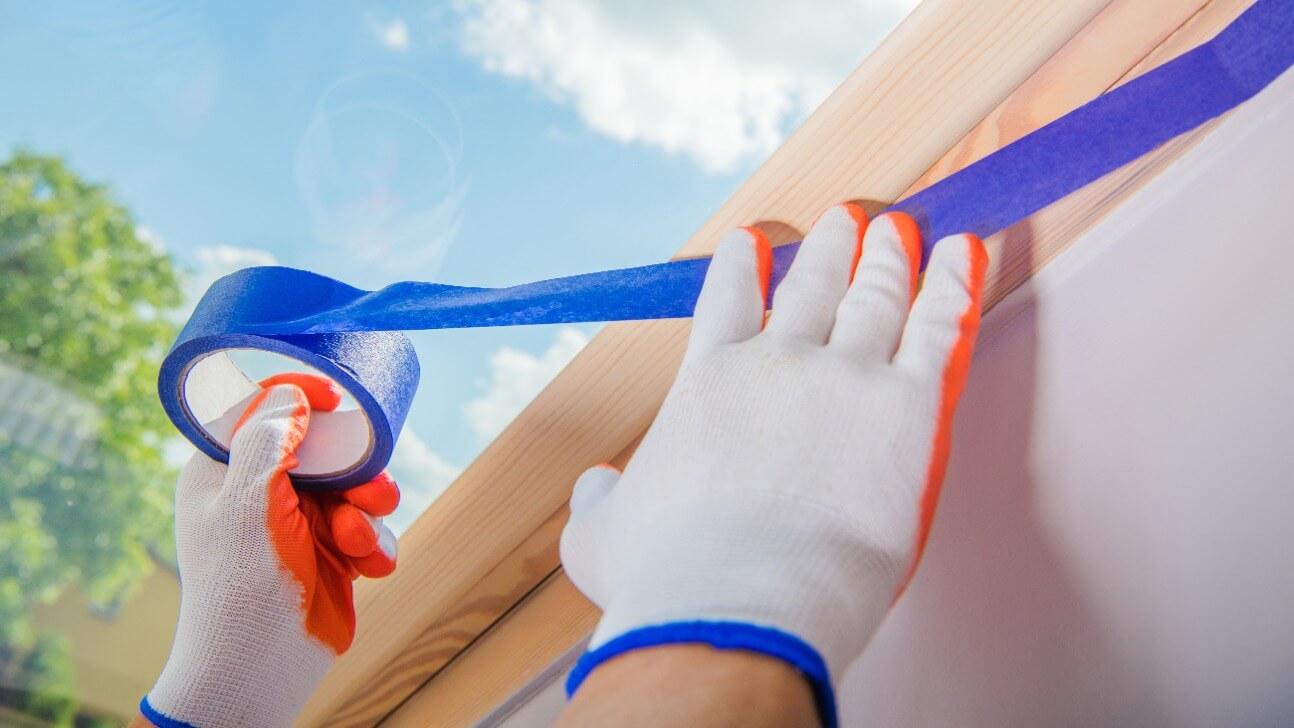 male construction worker applying painter s tape to a wall