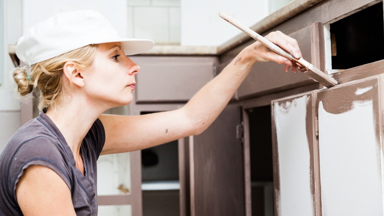 closeup of woman painting kitchen cabinets