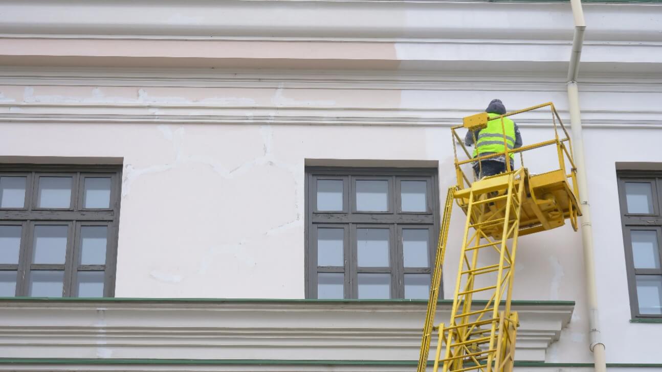 painters standing on aerial ladder paint the wall on