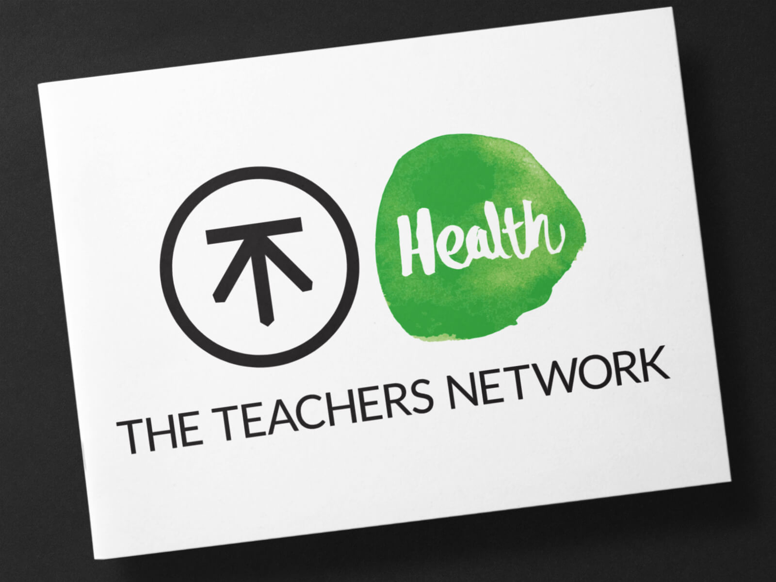 mock-up of The Health Teachers Network identity design printed on to a white business card with a deep grey background