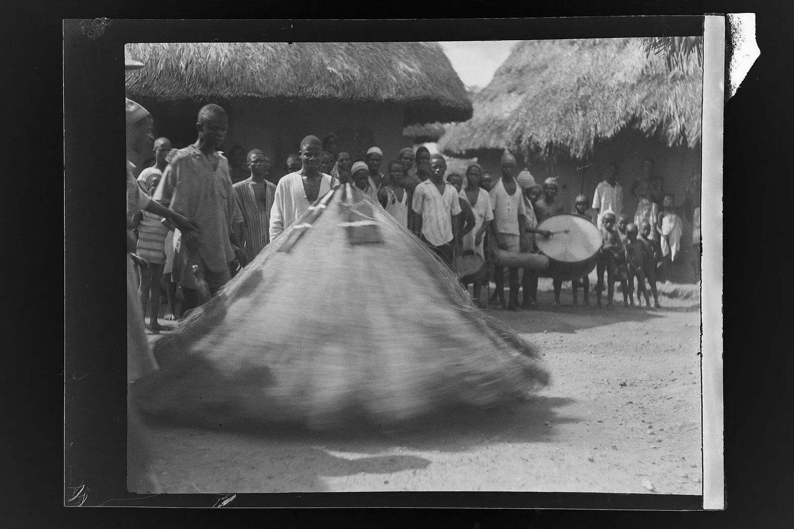Masked 'gbini' dancer, Panguma 1936, man playing drum to the right while others look on