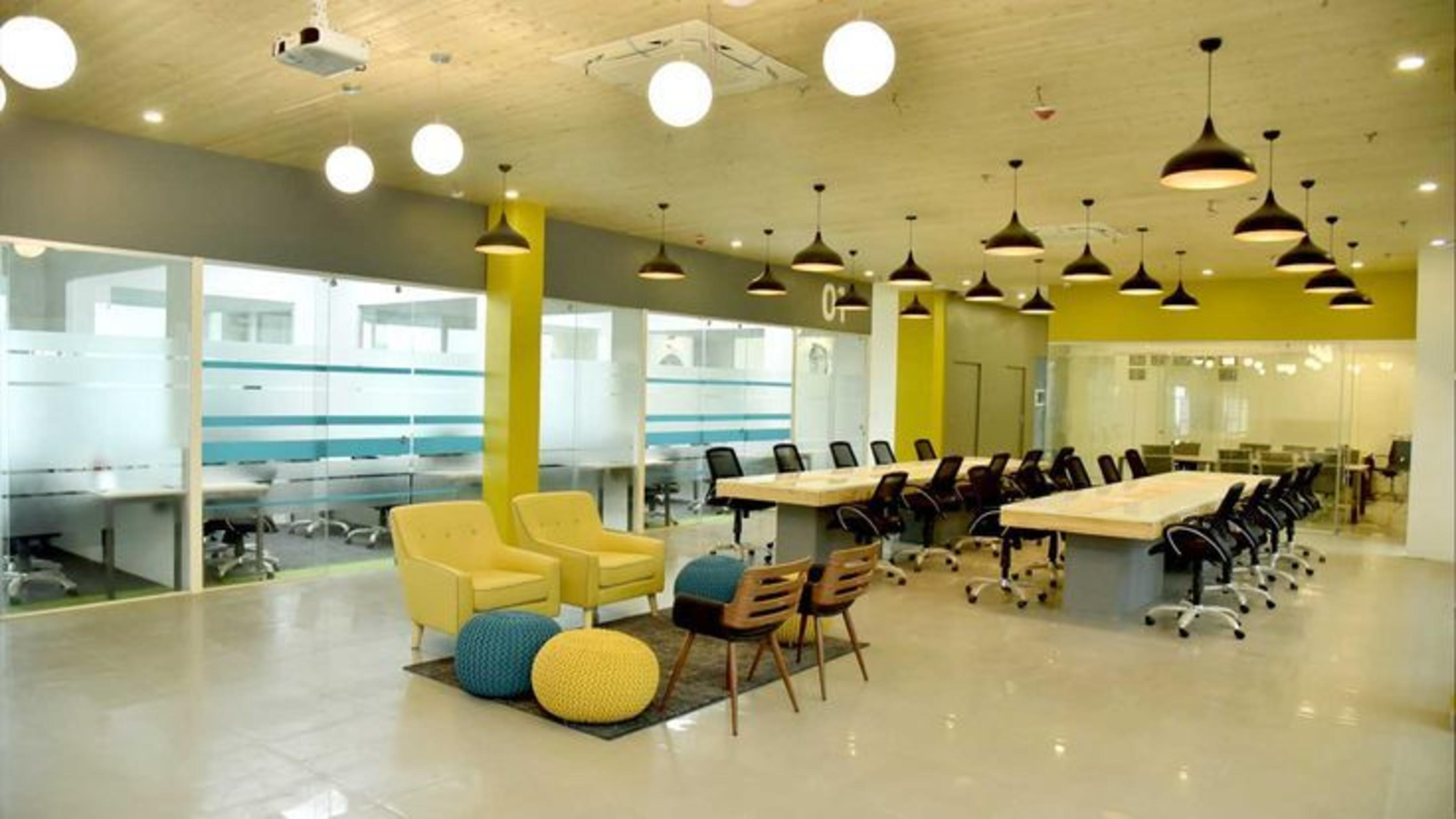 Conference room in Bangalore featuring large desks surrounded by black office chairs, light yellow sofas and ambient lighting