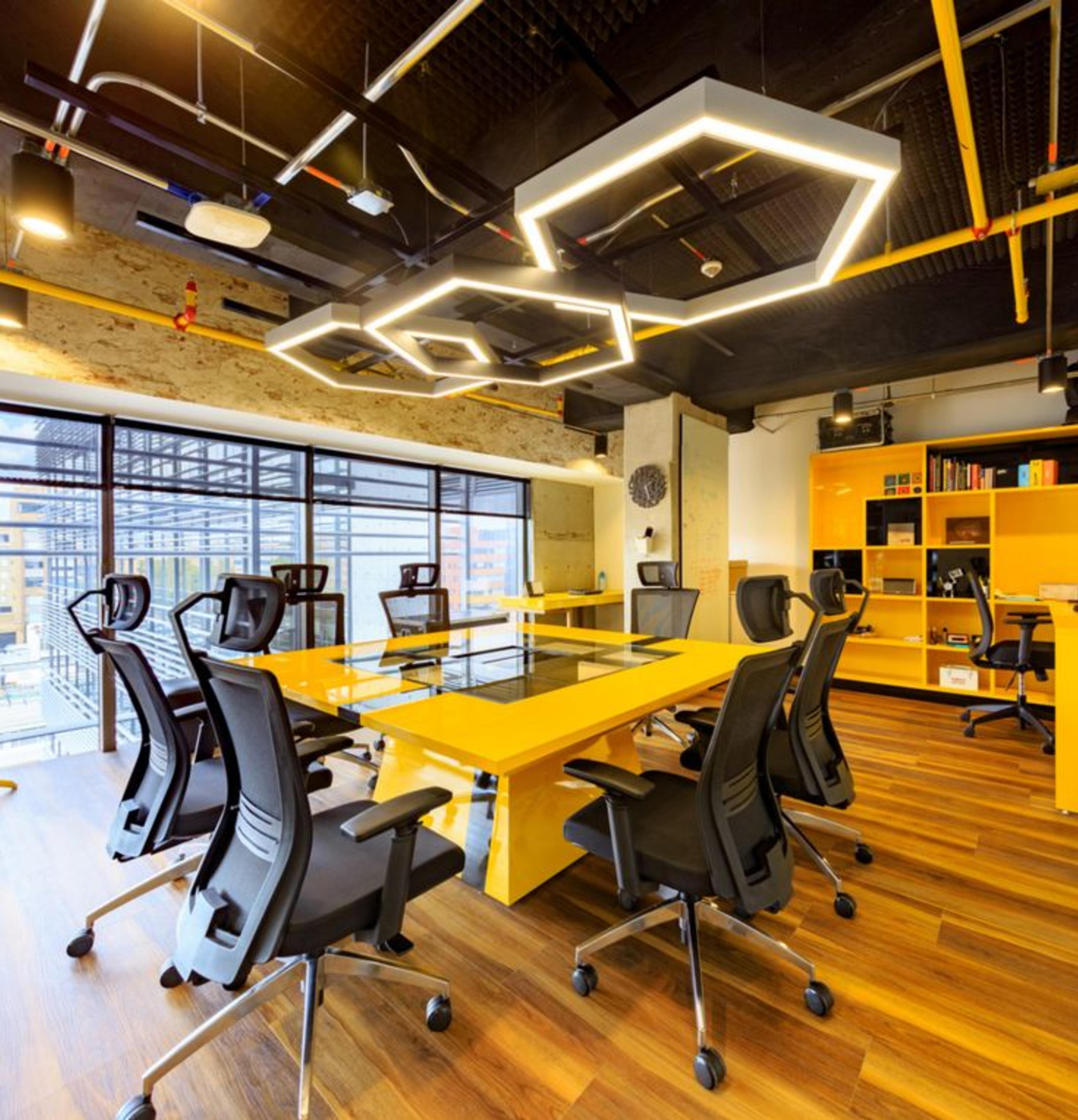 Private Office Space Rental in HSR Layout featuring a desk with black chairs yellow and white interiors and city view through glass walls