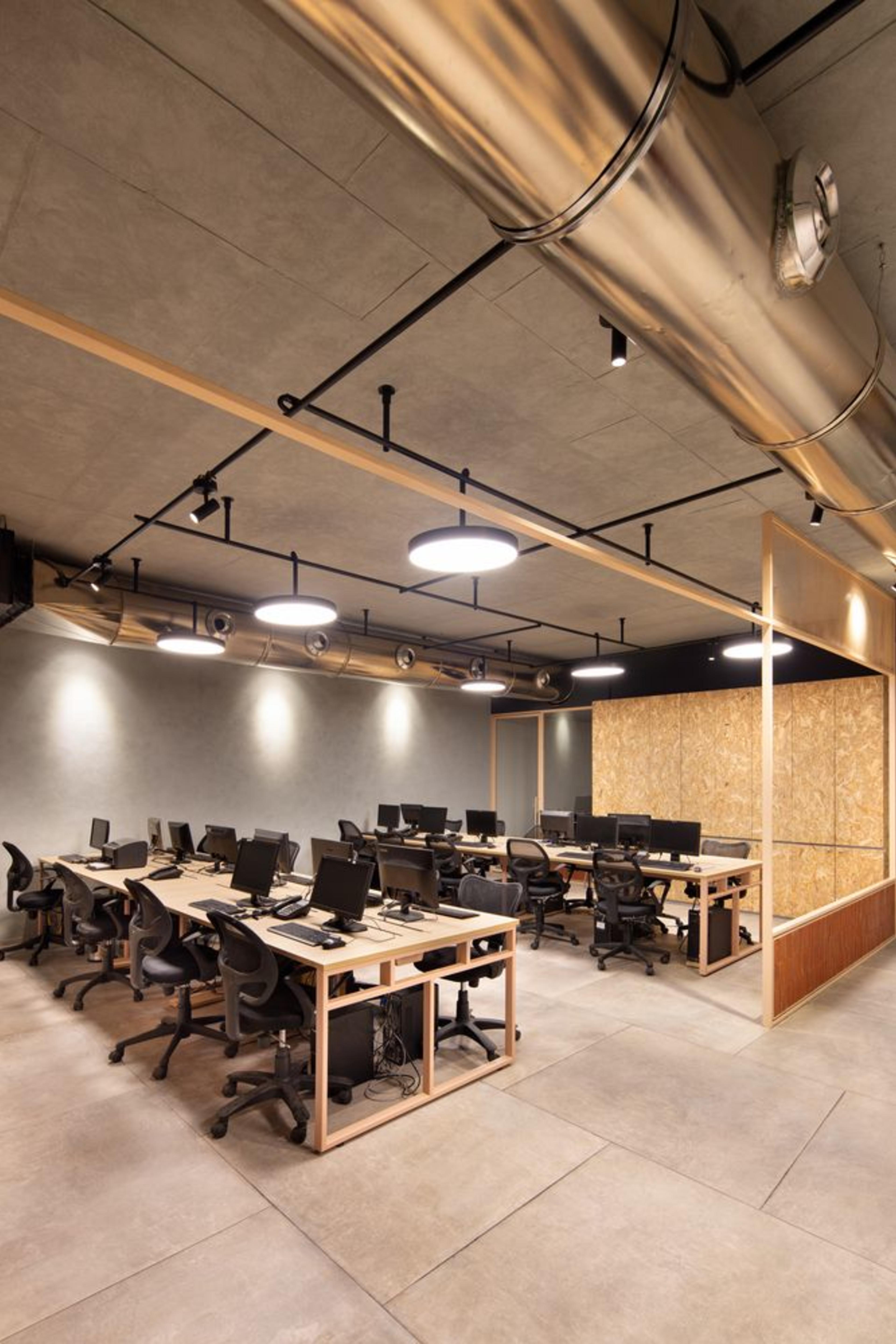 Black chairs placed around wooden desks in a managed office space in Bangalore featuring glass walls and warm lighting