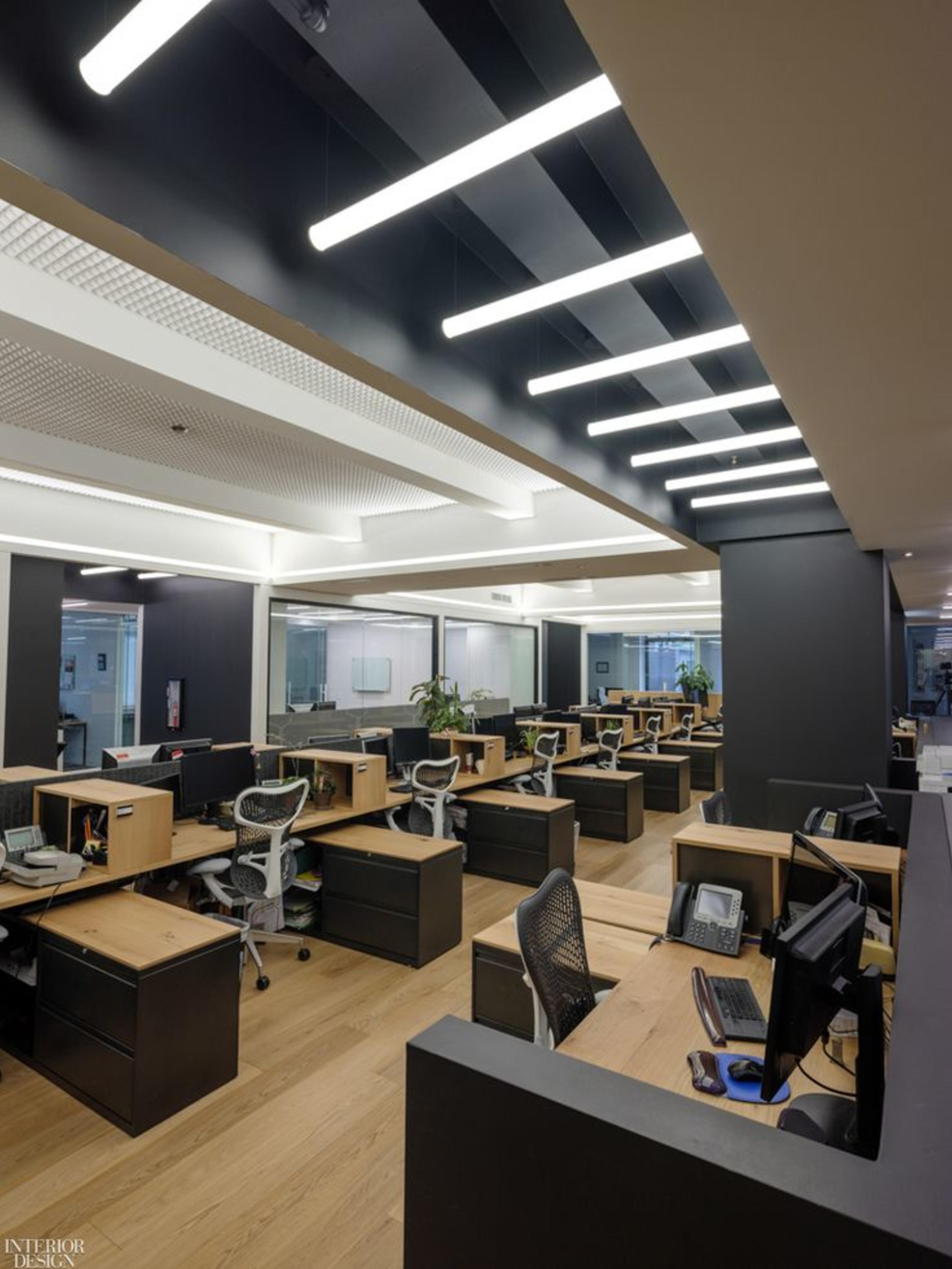 Hot desks for rent with wooden desks arranged throughout a modern workspace featuring green plants and glass partitions