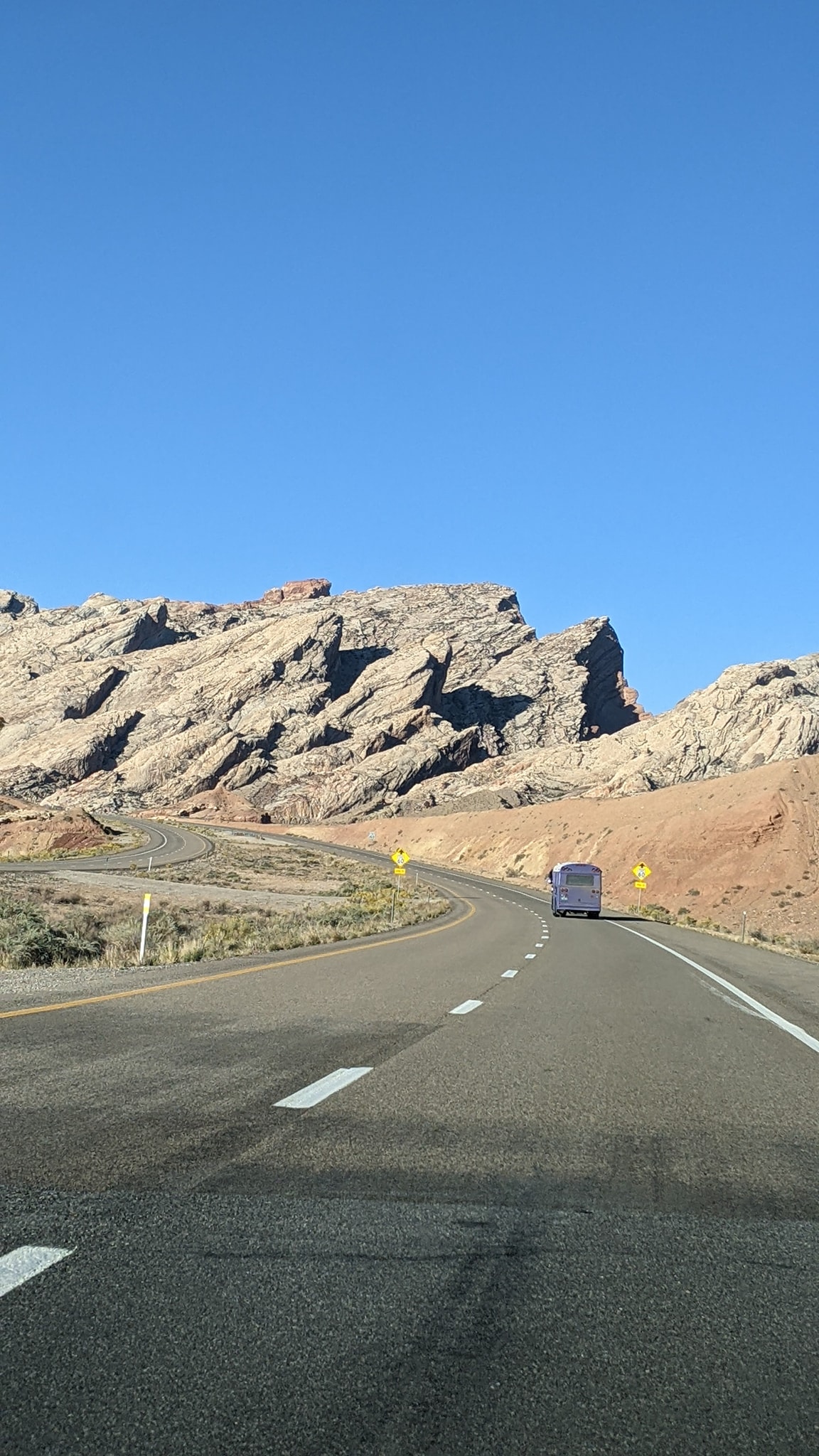 Skoolie Driving Past Huge Rock Formation in Desert
