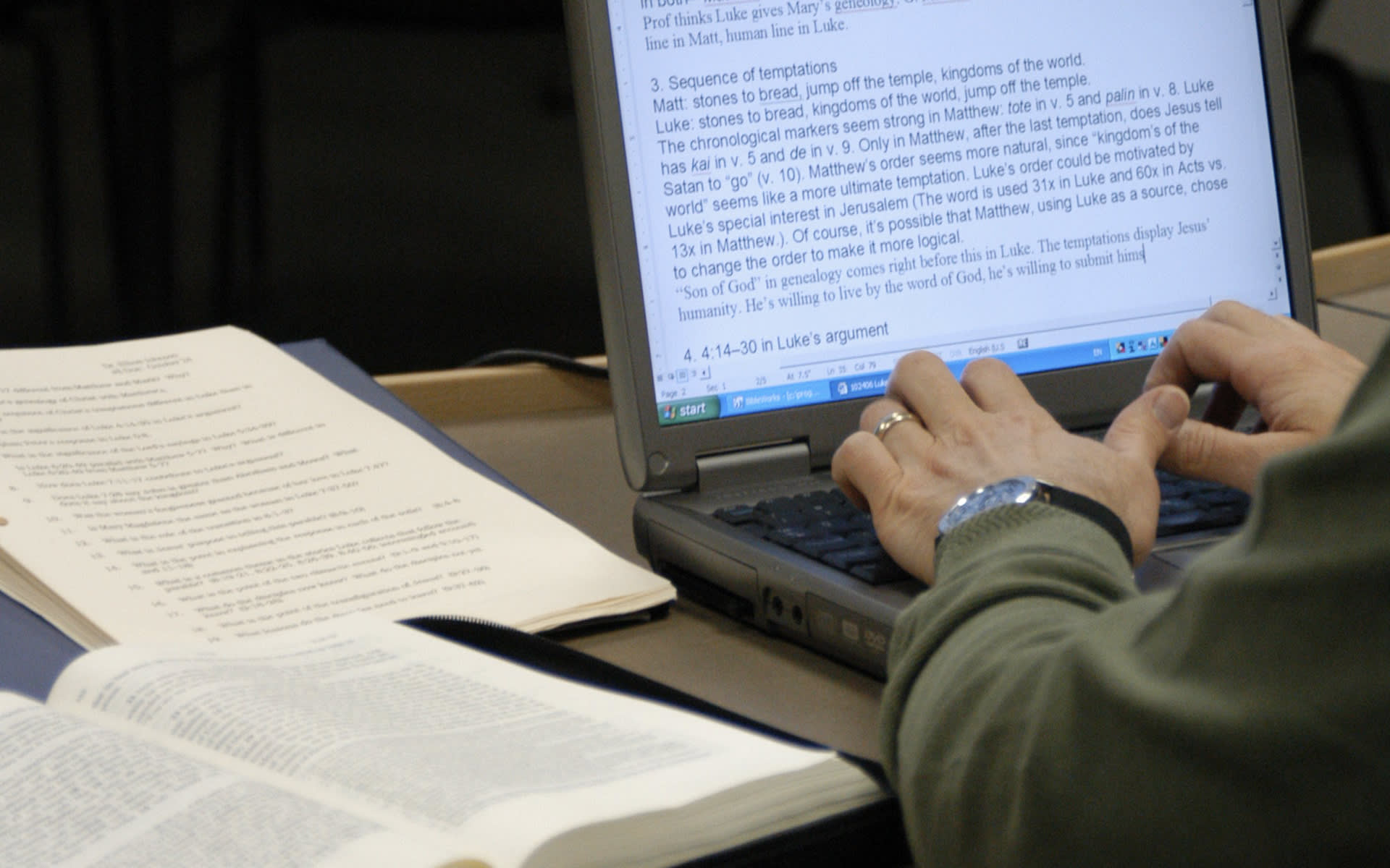student working on a laptop next to a pile of books