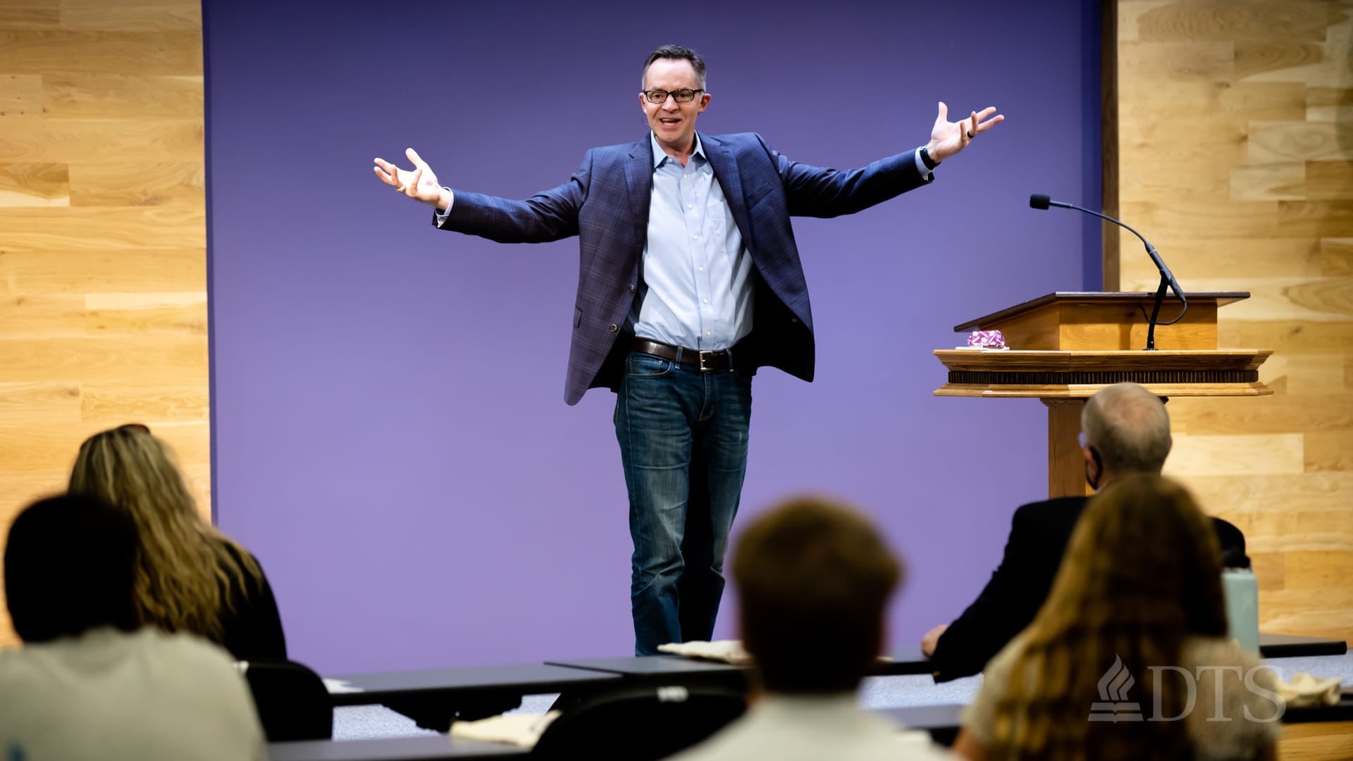 Dr. Brian Fisher, senior pastor of Grace Bible Church, standing in chapel with arms outstretched