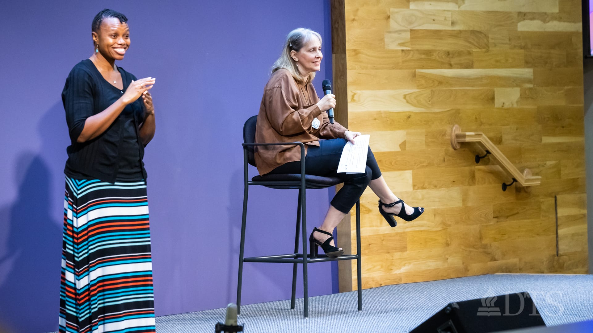 Dr. Sandra Glahn sitting on a tall chair and Ayokor Adjei standing beside her as the American Sign Language interpreter