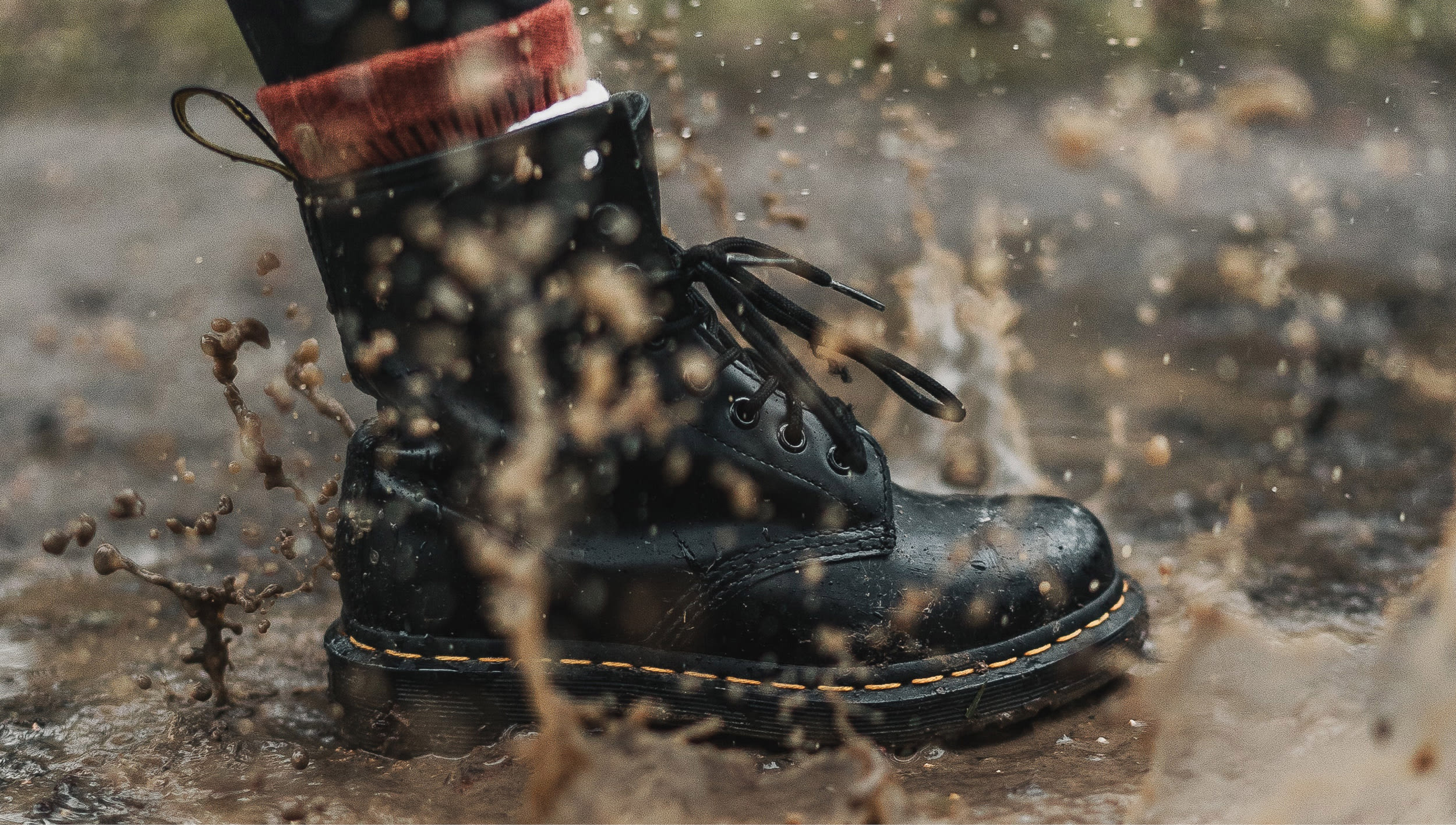 Black combat boot stepping into a mud puddle