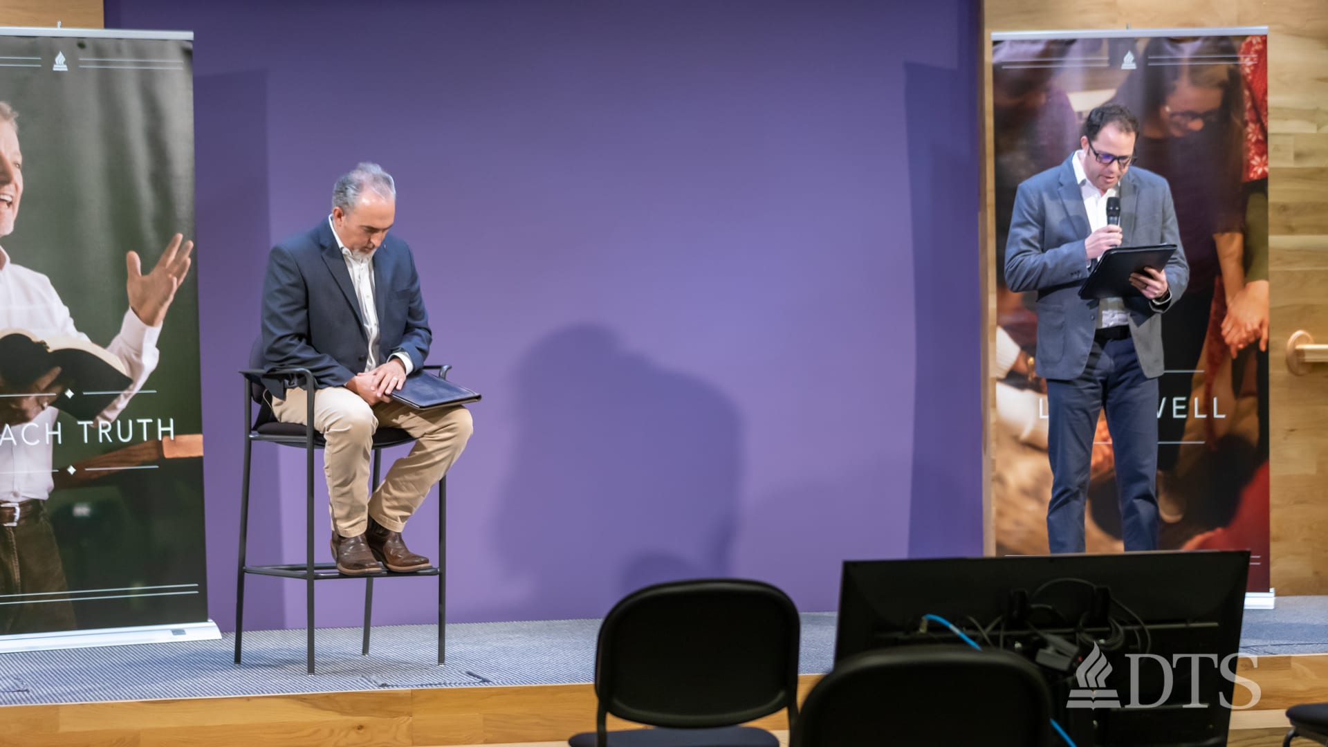 Dr. Mark Yarbrough seated on a stool with his head bowed while another man speaks