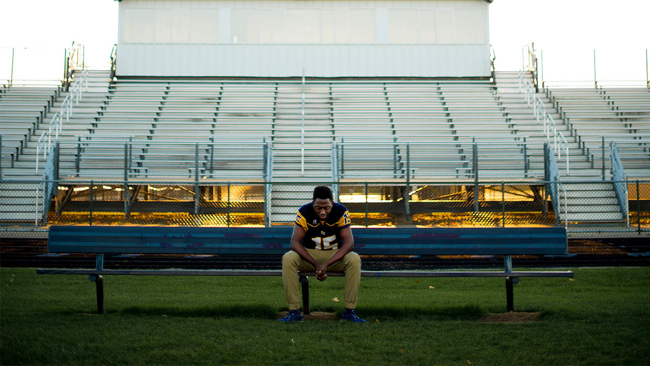 Young man seated on bench at a football field with empty stands behind him