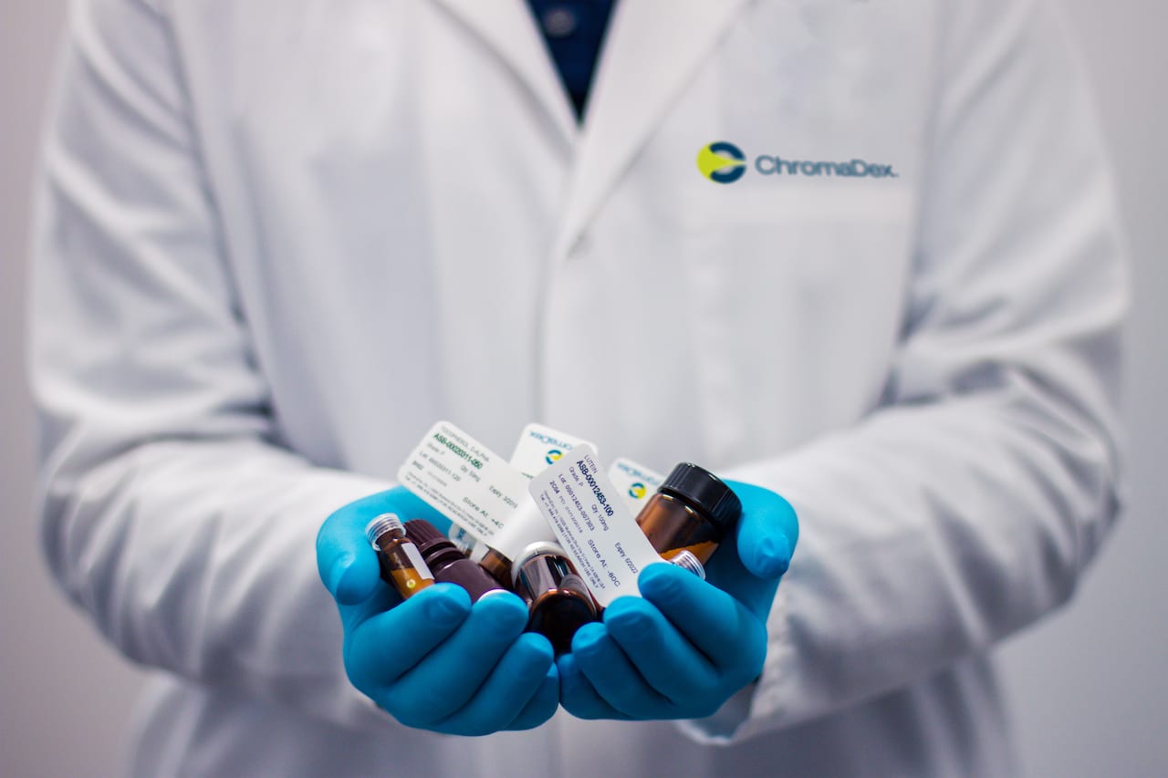 Personal in white coat and protective gloves holding medications