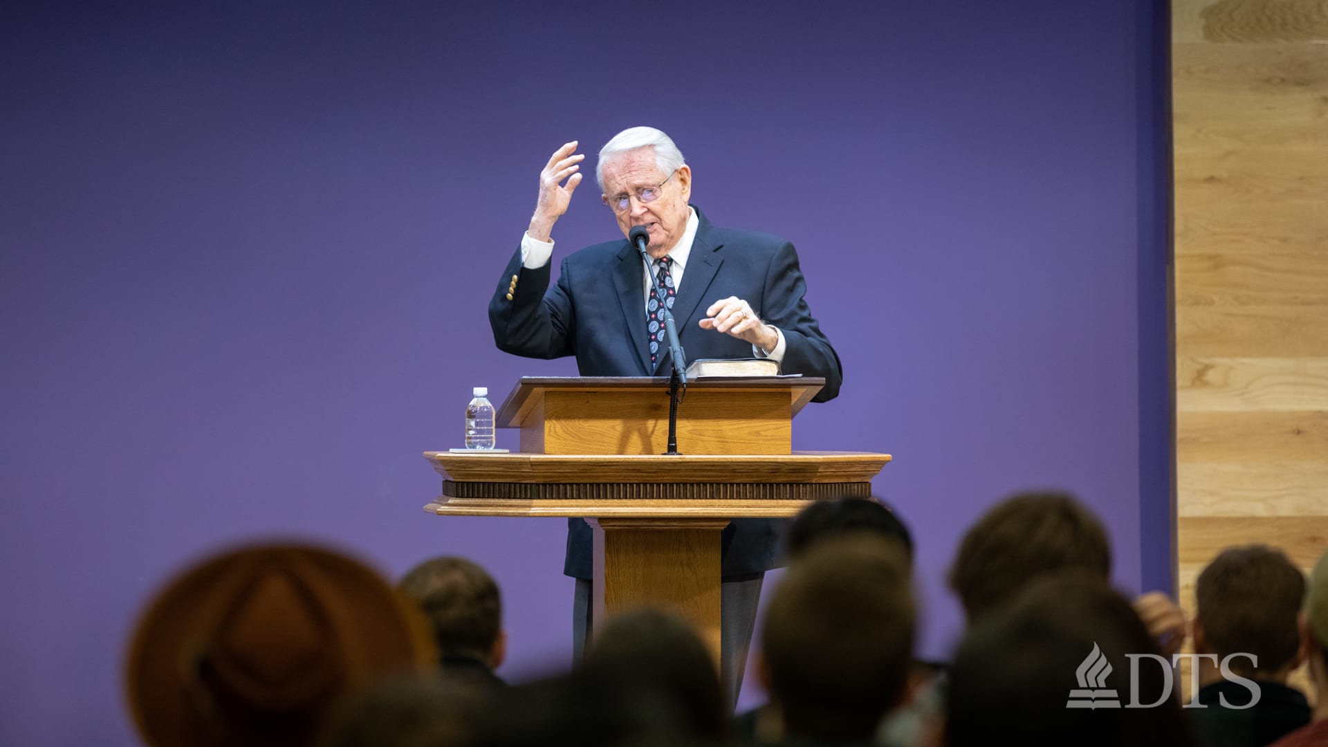 Dr. Chuck Swindoll standing at podium with hand raised while speaking at DTS Chapel