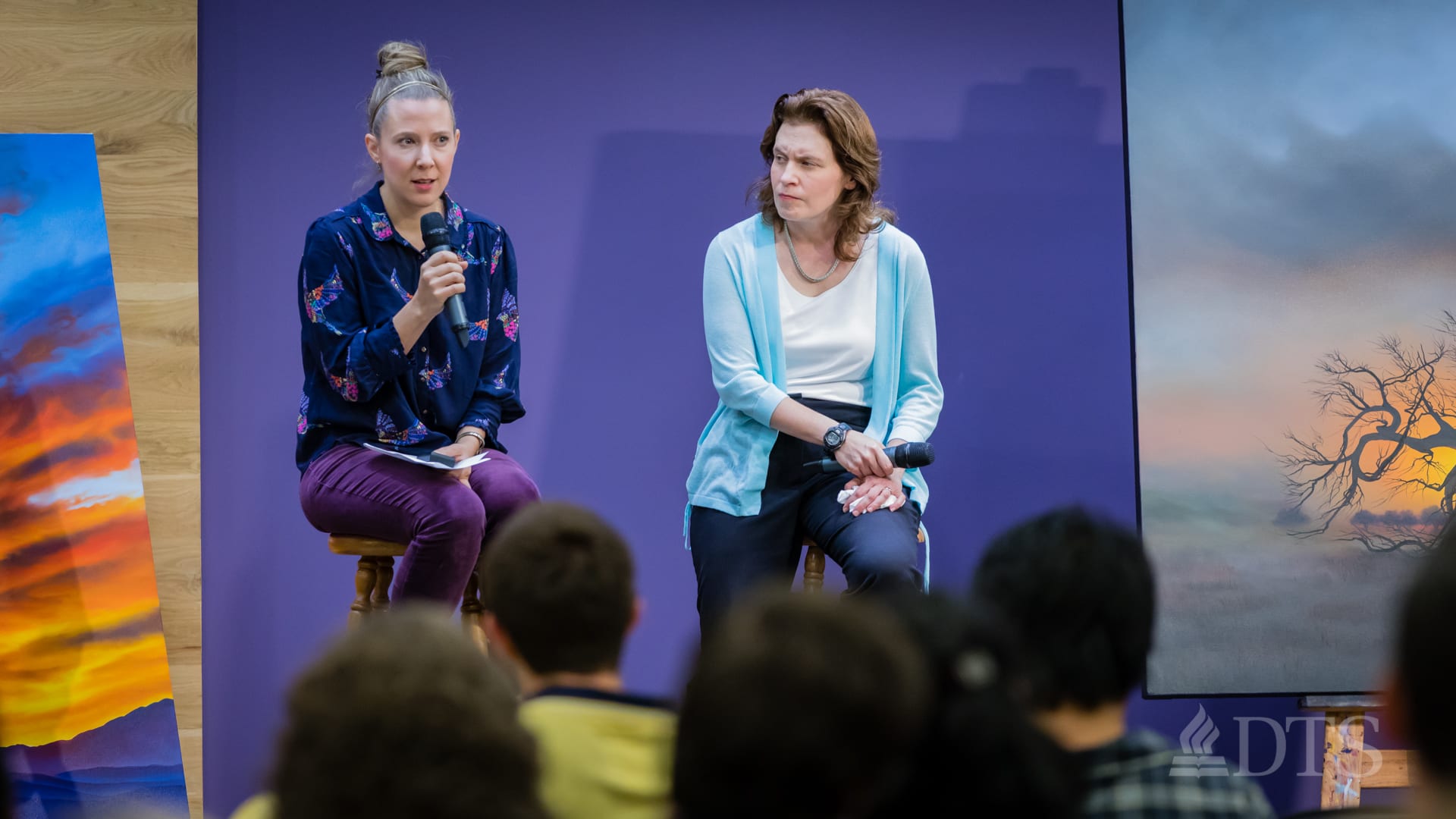 two women seated on stools on stage while speaking at DTS Chapel