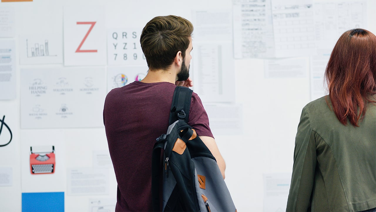 Woman and man standing in front of a wall filled with bulletins to read