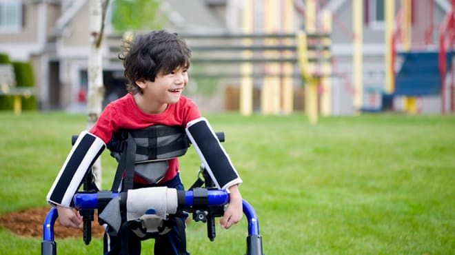 Young boy smiling while using mobility equipment to play outside on a playground