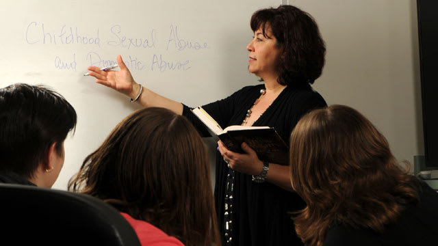 Woman pointing to whiteboard while teaching a group of women in a classroom