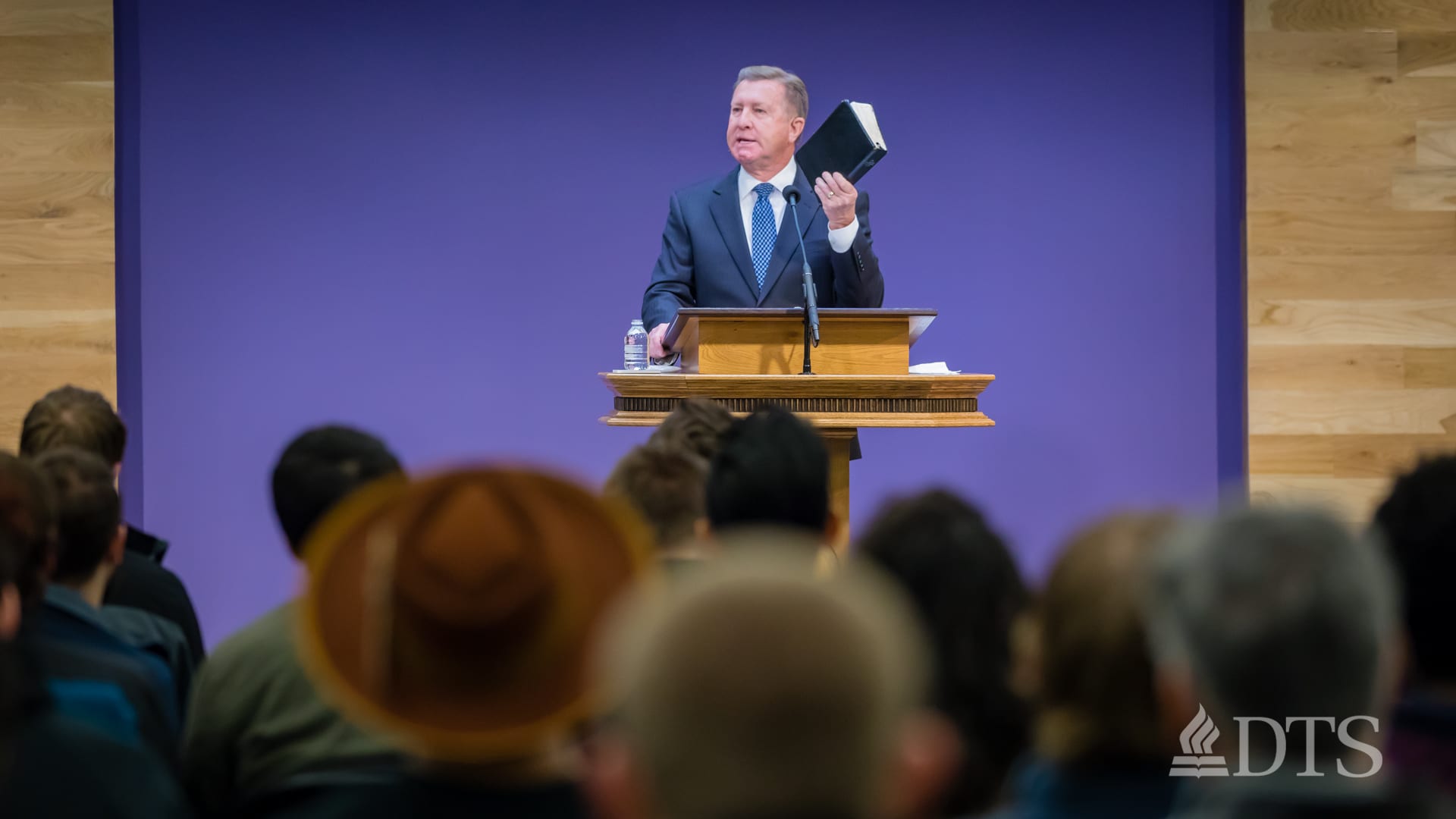 man standing at podium holding his Bible in the air while speaking at DTS Chapel