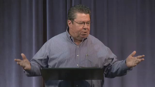 Dr. Mark Bailey standing at a podium with arms outstretched while speaking