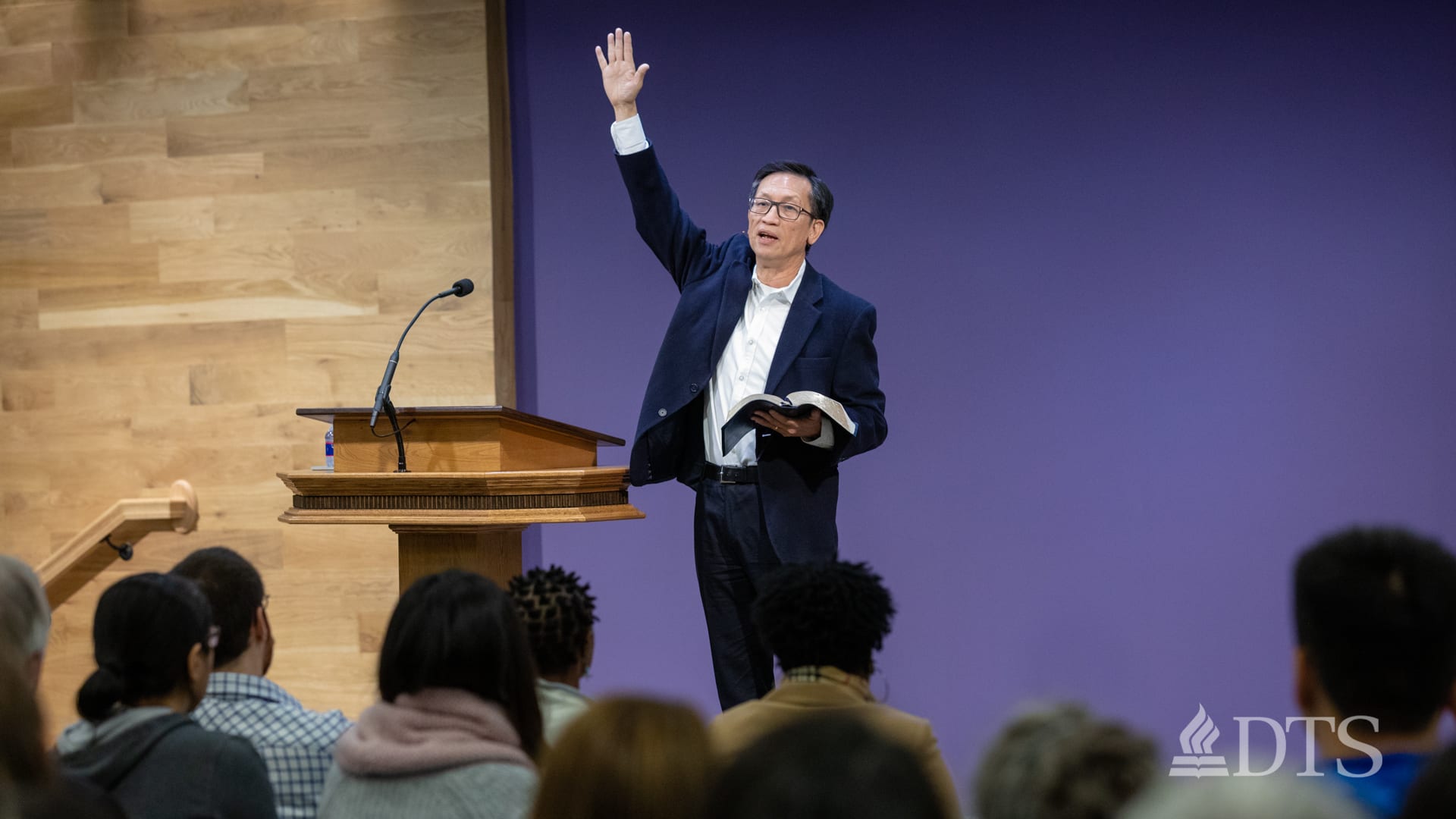 man standing near podium with hand raised while speaking at DTS Chapel
