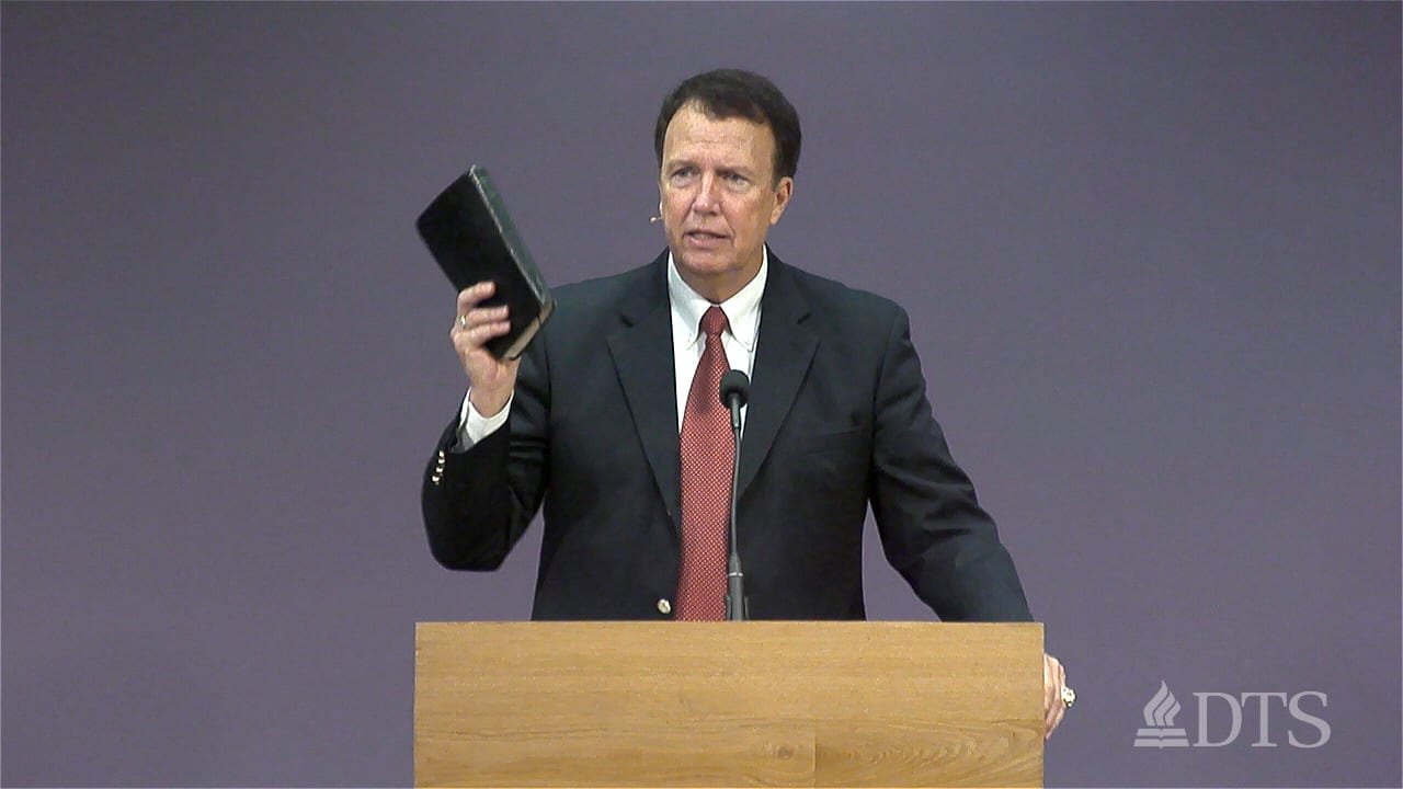 man standing at podium holding his Bible in the air while speaking at DTS Chapel