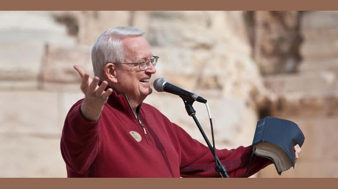 Dr. Swindoll standing at a podium holding his Bible and speaking into a microphone