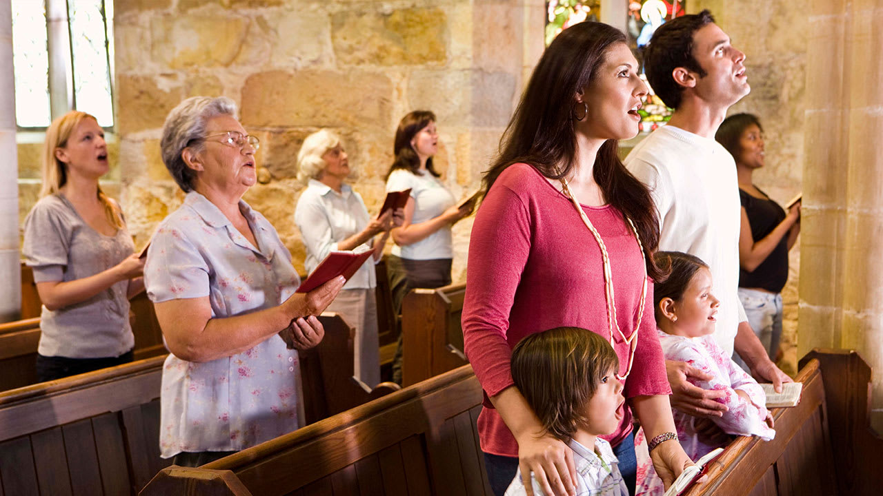 Congregation singing inside building with pews and stained-glass windows
