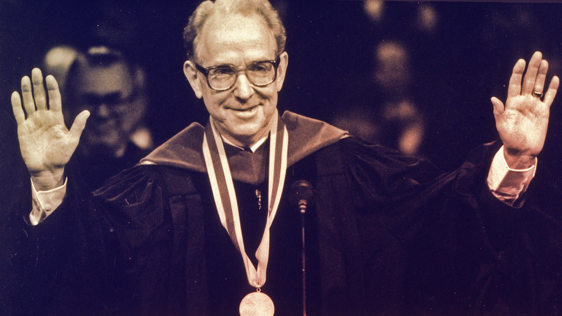 Dr. Campbell standing with hands outreached in regalia