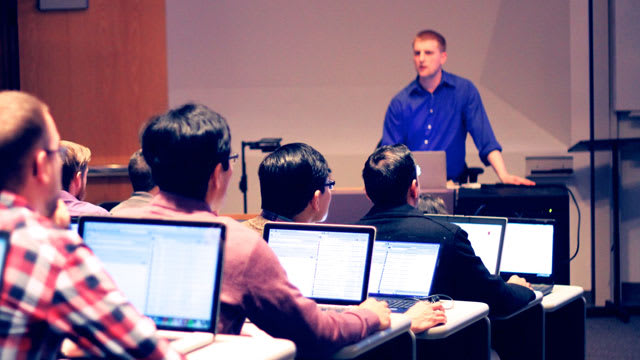 Man using laptop teaching full classroom of students also using laptops