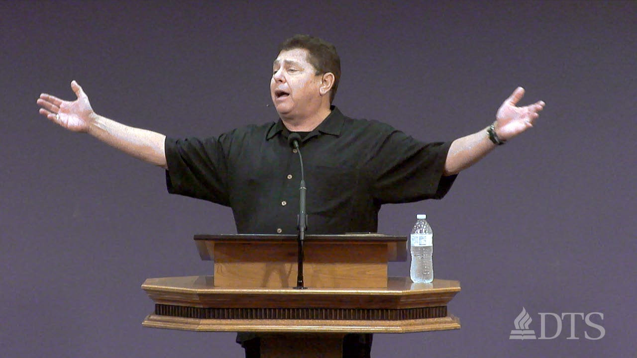 man standing at podium with arms upraised while speaking at DTS Chapel