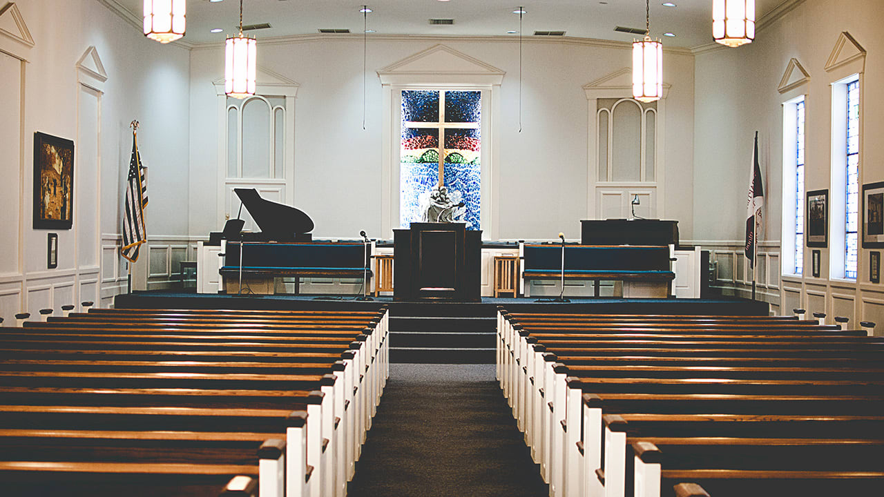Interior view of empty church sanctuary with wooden pews and stained glass window behind podium