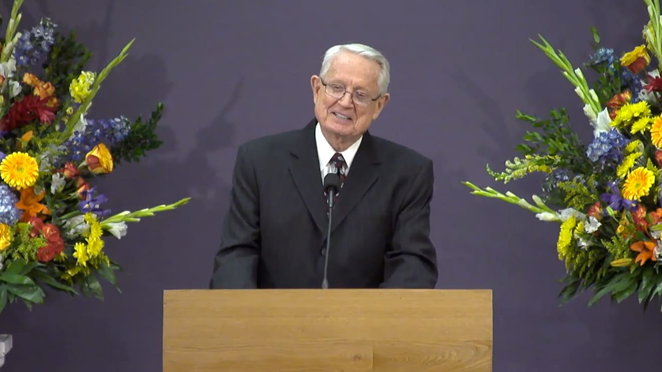 Dr. Swindoll speaking at a podium between two large floral bouquets
