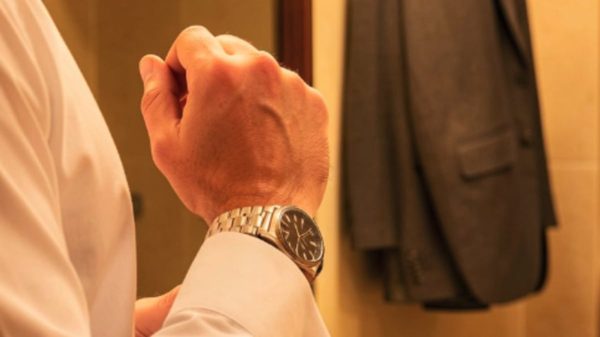 Hombre ajustándose el puño de la camisa frente al espejo, reloj en la muñeca, arreglándose con cuidado