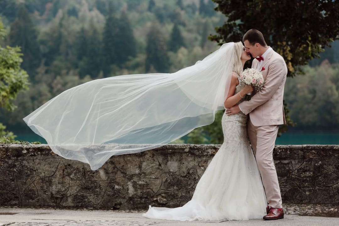 Couple kiss with a dramatic wind-blown veil on Bled island, signature Lake Bled moment.