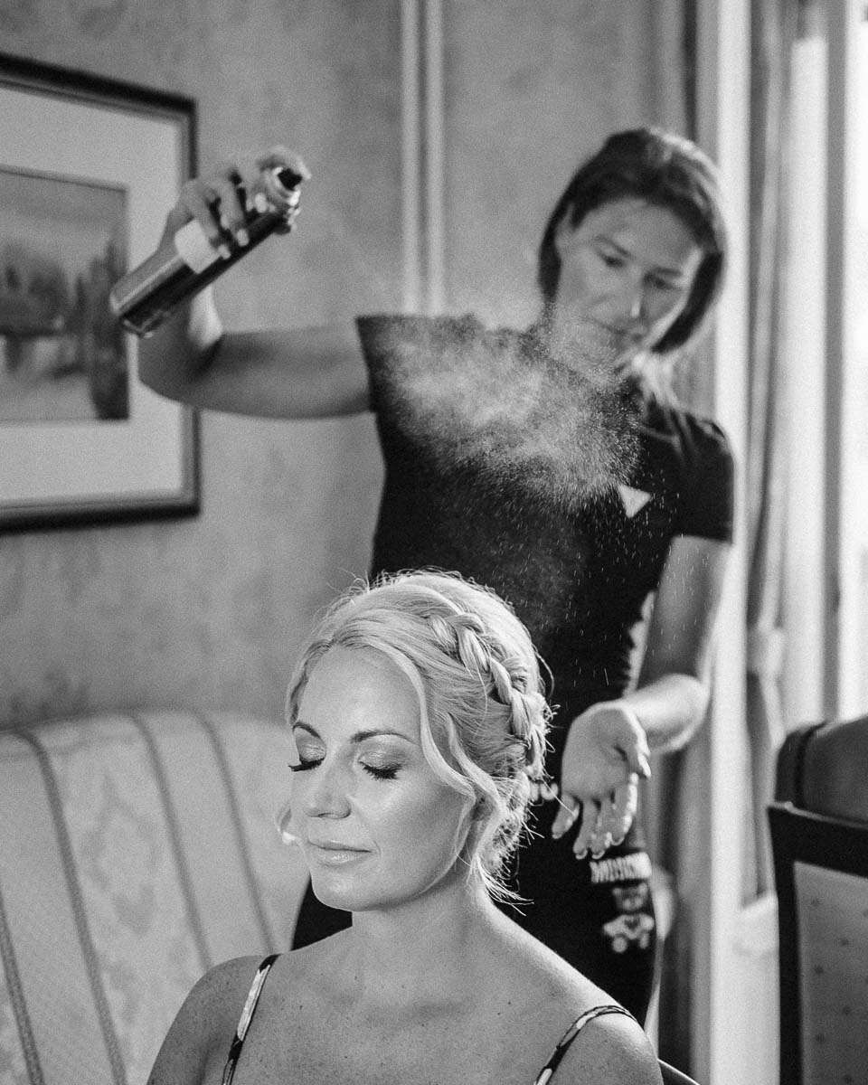 A bride getting her hair styled with hairspray being applied in a salon setting.