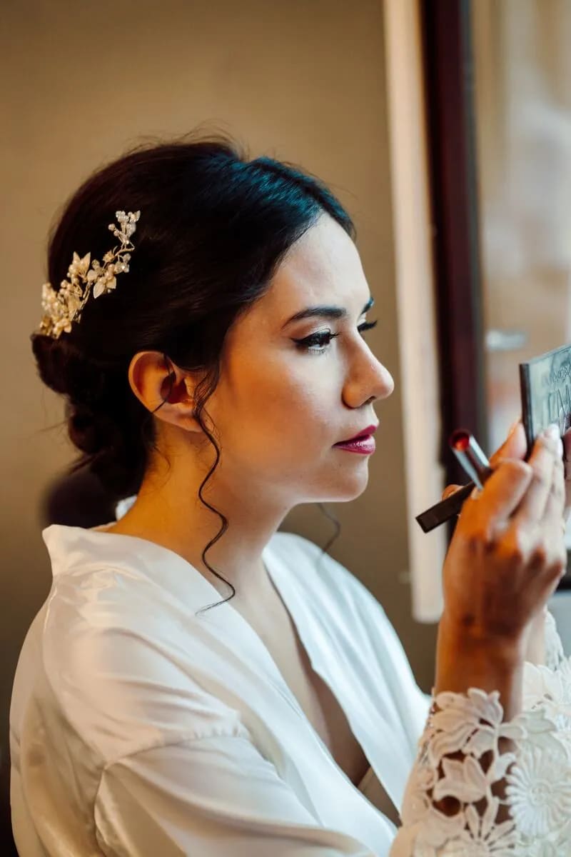 A bride applying makeup while wearing a white robe, preparing for her wedding day.