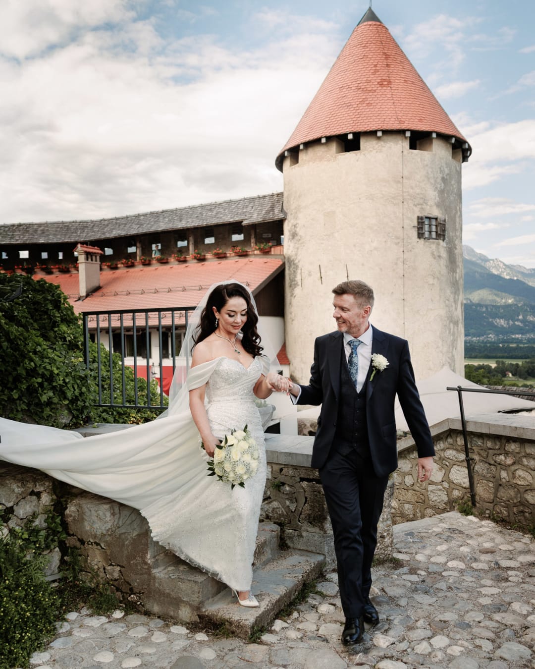 Couple walking at Bled Castle with the tower behind them.