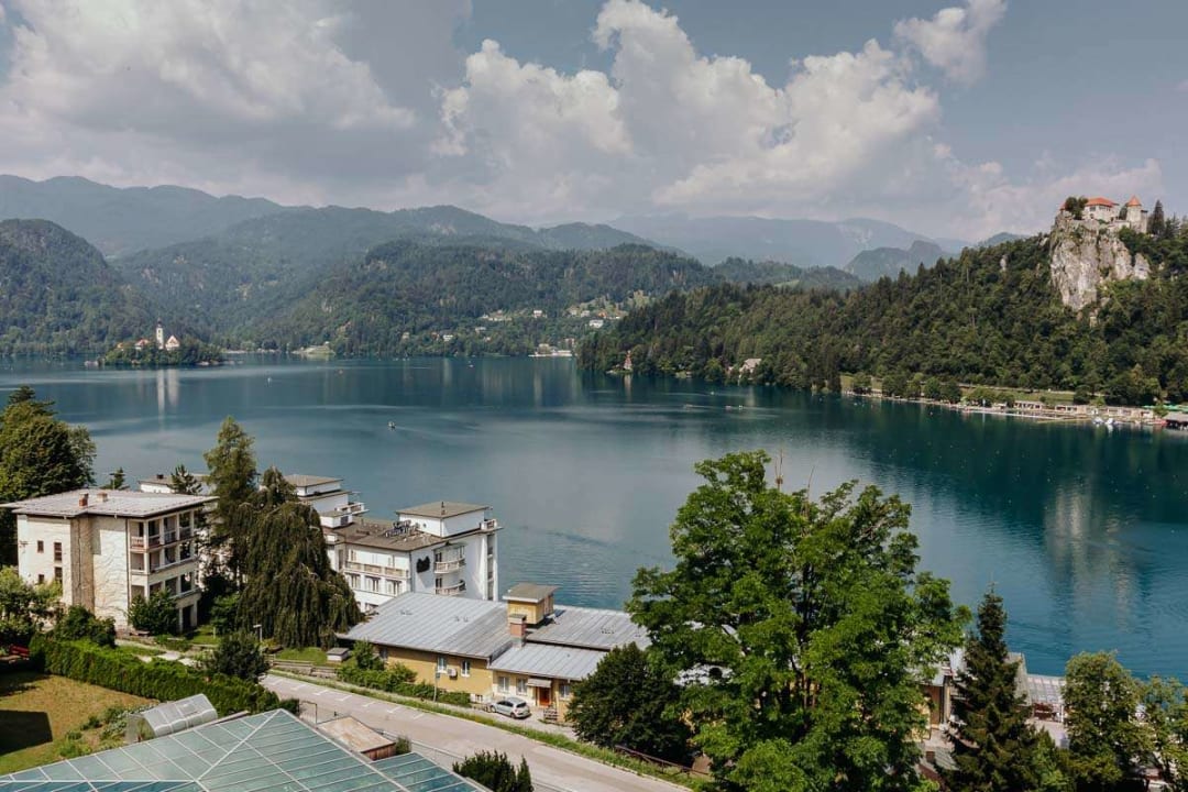 A scenic view of Lake Bled with its iconic castle on a hill and a church on an island, surrounded by mountains and lush greenery.