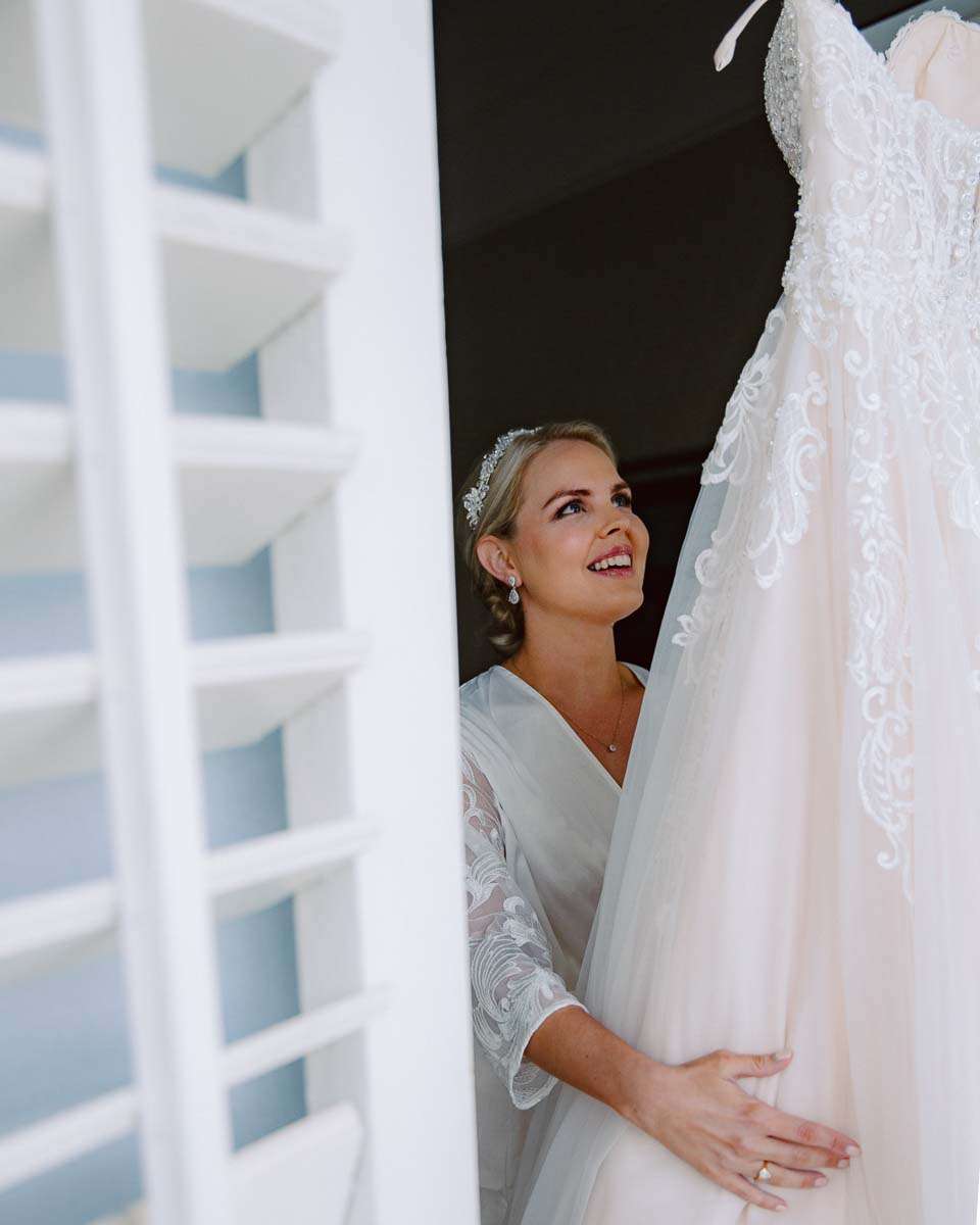 A bride smiling as she holds up her wedding dress, looking at it with admiration.