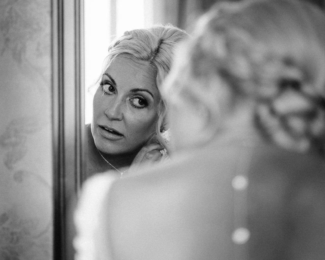 A bride looking into a mirror as she adjusts her earring while getting ready for her wedding.