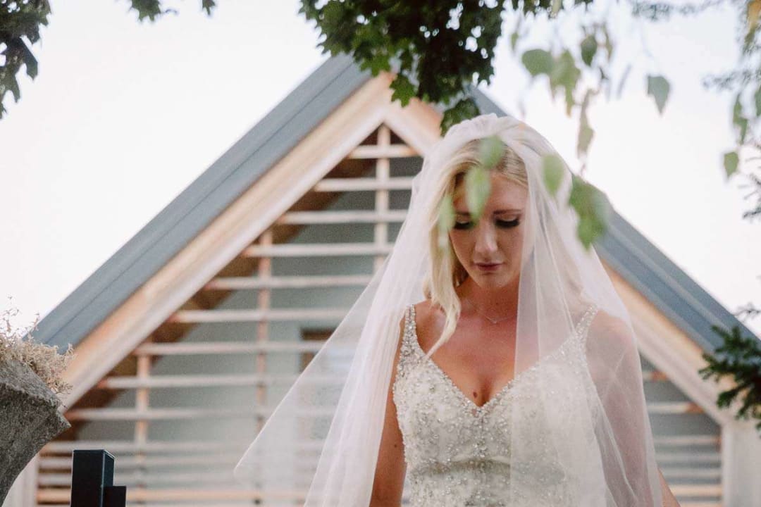 A bride in a beaded gown and veil standing pensively in front of a church entrance.