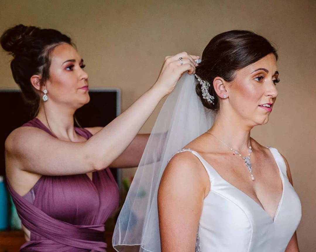 A bride is getting her veil adjusted by a bridesmaid before the wedding ceremony.