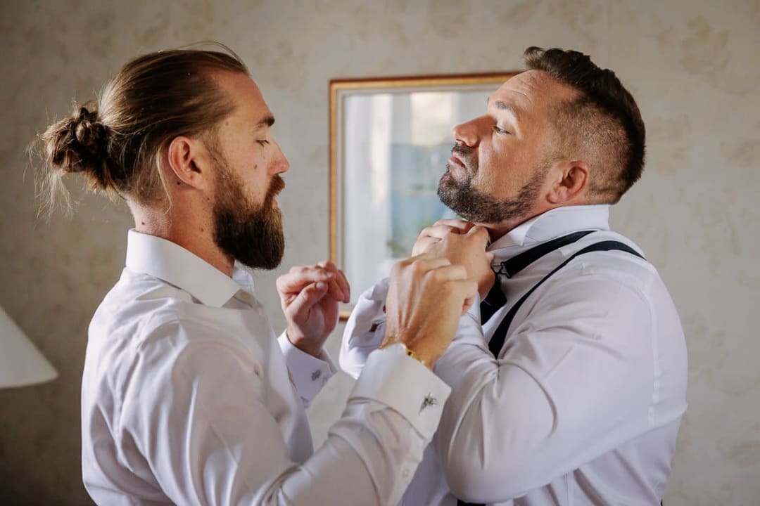 A groom getting help with his collar from a friend while preparing for the wedding day.