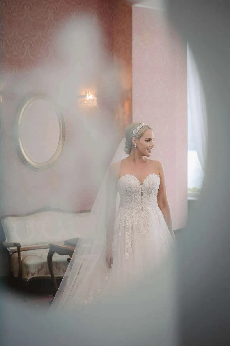 A bride in a beautiful lace gown standing in an elegantly decorated room with soft lighting.