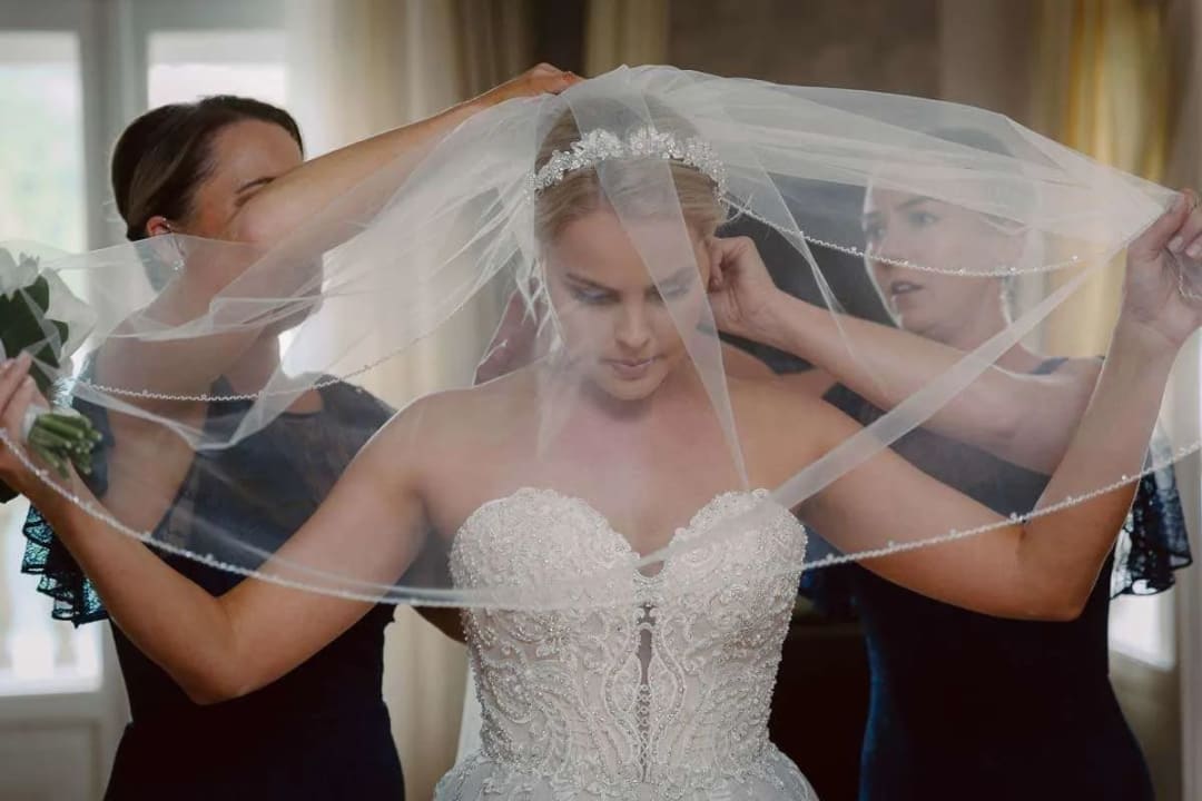 A bride getting ready as two bridesmaids help her adjust her veil.