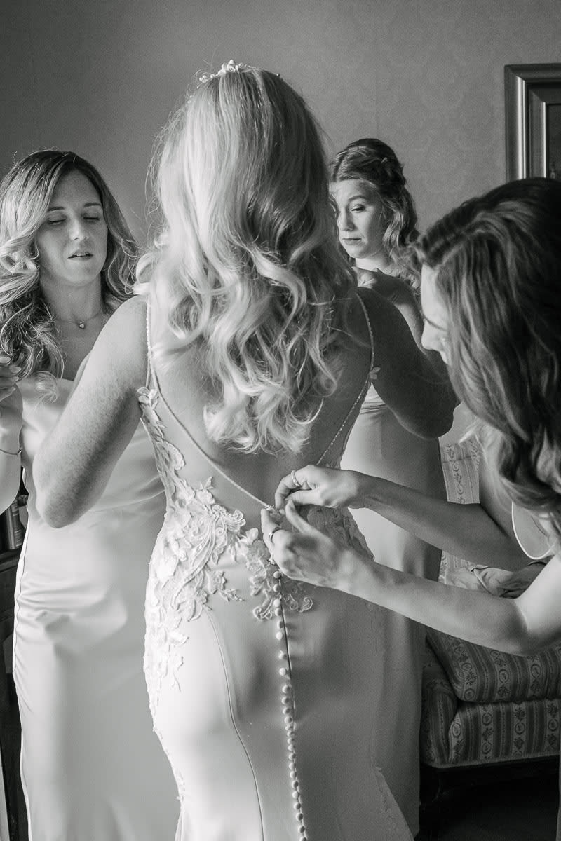 A bride being assisted by her bridesmaids as they button up her wedding dress.