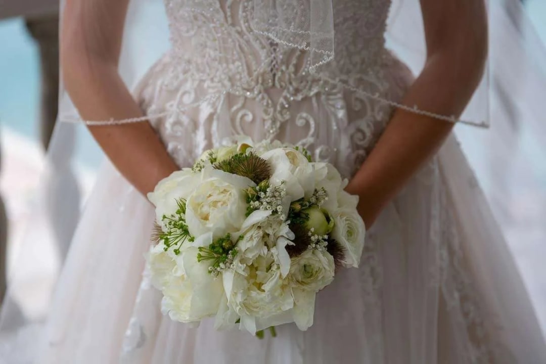 Close-up of a bride holding a bouquet of white flowers, showing the intricate detail of her wedding dress.