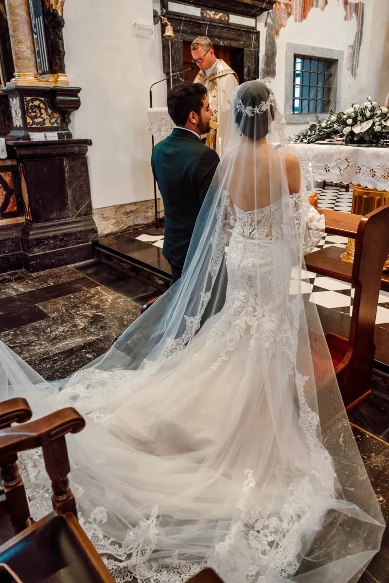 A bride and groom kneeling at the altar during a church ceremony with the priest in front of them.