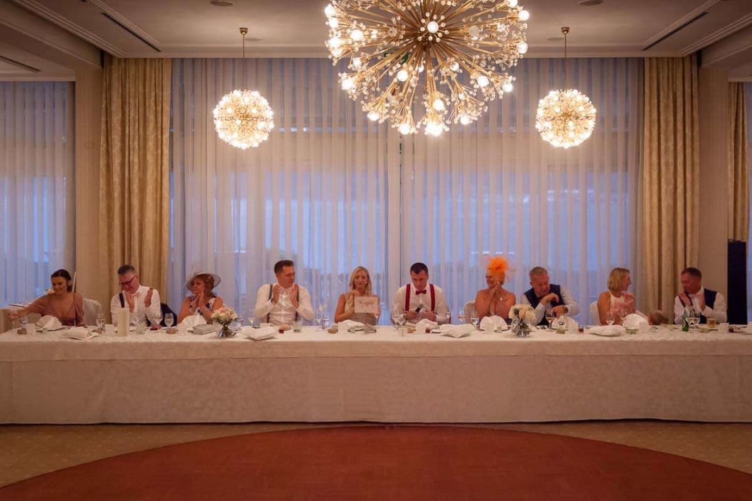 A long table set for a wedding reception with guests sitting and chatting under elegant chandeliers.